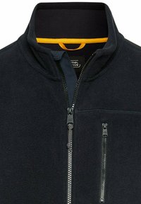 Fleecejacke in Dunkelblau, mit hohem Kragen, schwarzen Reißverschlussöffnungen und orangefarbenem Innenfutter. Mit einer zipbaren Brusttasche.