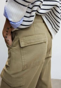Pantaloni cargo color khaki con due grandi tasche posteriori, realizzati in un tessuto resistente. La vita presenta un design robusto per funzionalità e vestibilità.