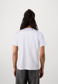 Valkoinen puuvillainen lyhythihainen t-paita, jossa pyöreä pääntie ja rento istuvuus. Selkäpuoli on yksivärinen, ilman näkyviä logoja tai kuvioita.