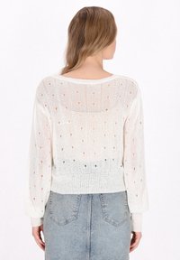 Pulover tricotat din crem cu un model deschis de puncte, cu manșete și talie ribbate. Textură moale, croială lejeră și design ușor pentru o bună respirabilitate.