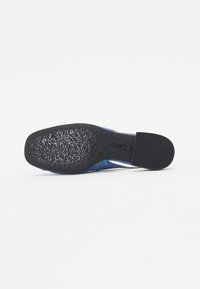 Semelle de chaussure bleue montrant une semelle en caoutchouc noire avec un motif floral orné et le nom de marque Gabor, taille 4 ½, sur fond blanc.