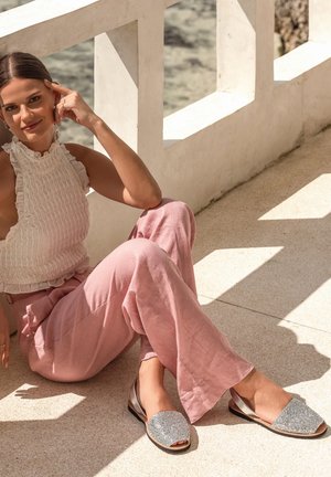 Chaussures argentées scintillantes à enfiler avec un bout arrondi, associées à un pantalon large en lin rose pâle et un haut texturé blanc.