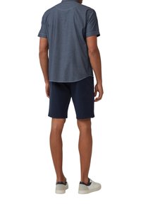 Korte mouwen, donkerblauwe chambray overhemd met een gebogen zoom, gedragen met marineblauwe shorts en witte sneakers. Schoon ontwerp, geen zichtbare patronen.