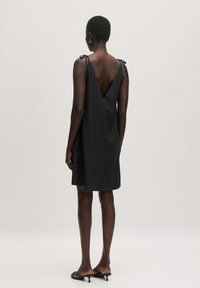 Zwart mouwloos jurkje met een diepe V-rug, verstelbare schouderbandjes en zachte stof. Valt boven de knieën, minimalistisch ontwerp, elegante silhouet.