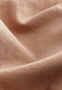 Tessuto morbido e intrecciato di un leggero colore pesco, con una texture liscia e un delicato motivo diagonale, mostrato in pieghe ondulate.