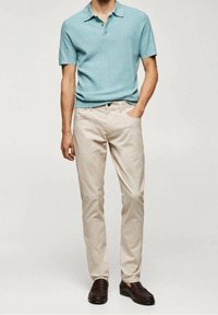 Lichtblauwe poloshirt met korte mouwen en ribbelstructuur, beige rechte chino's, en donkerbruine instapschoenen.