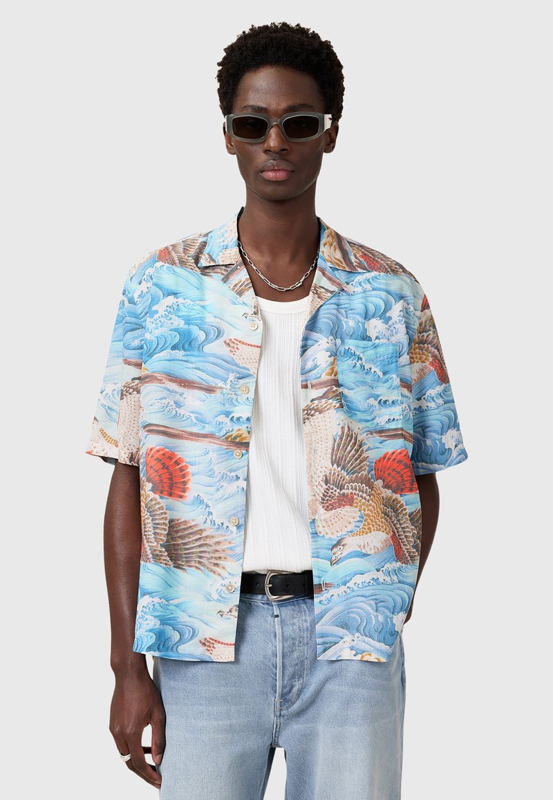 Kurzärmliges Hemd mit Knopfverschluss, das ein blaues Ozeanwellenmuster mit roten und orangefarbenen Akzenten zeigt und eine entspannte Passform hat. Kombiniert mit hellblauen Jeans.