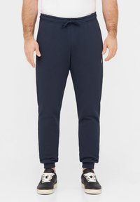 Marineblaue Jogginghosen mit einem elastischen Bund, Kordelzug und gerippten Bündchen. Kombiniert mit schwarzen Sneakers mit weißen Schnürsenkeln.