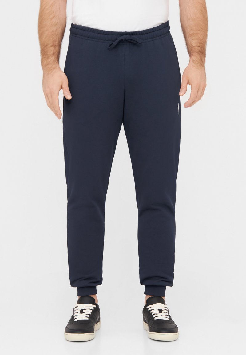 Marineblaue Jogginghosen mit einem elastischen Bund, Kordelzug und gerippten Bündchen. Kombiniert mit schwarzen Sneakers mit weißen Schnürsenkeln.