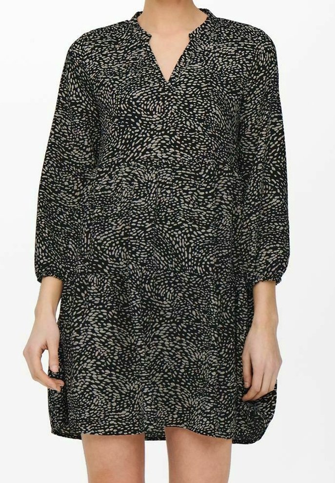 Robe longue à manches longues noire avec motif de points abstraits beiges, encolure en V et jupe ample à volants portée par une personne debout.