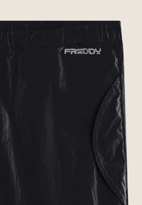 Schwarze Sporthose mit elastischem Bund, Seitentasche und silbernem, gesticktem "FREDDY"-Logo nahe dem oberen Rand.