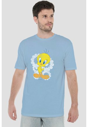 Mann trägt hellblaues T-Shirt mit großer Grafik von Tweety Bird, der in einem weißen Blumenmuster steht.