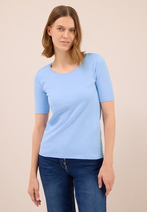 Světle modrá košile s krátkým rukávem a kulatým výstřihem, vyrobená z měkké látky, s přiléhavým střihem a hladkou texturou. Nositá s modrými džíny.