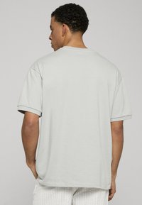 Svetlo šedé tričko s krátkym rukávom a voľným strihom, s okrúhlym výstrihom a prehnutými rukávami. Hladká bavlnená textúra.