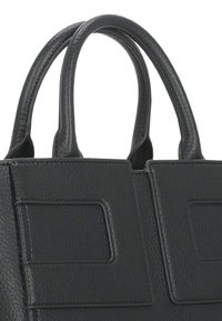 Czarna skórzana torebka o zdefiniowanym kształcie, z dwiema okrągłymi uchwytami i minimalistycznym wzornictwem, z kwadratowymi akcentami z przodu.