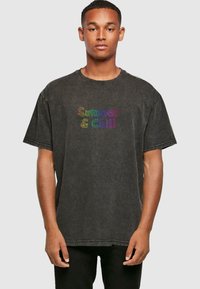 Camiseta oversized de algodón negra con texto multicolor "Summer & Chill" en la parte frontal, con escote redondo y mangas cortas.