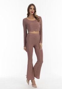 Twee-delige outfit bestaande uit een cropped longsleeve top en uitlopende broek in een glanzende rozenkleur, gemaakt van een zachte, rekbare stof.