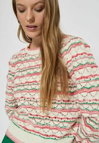 Strickpullover mit einem cremefarbenen Grund, der rote und grüne Zickzackmuster aufweist. Das Design umfasst eine offene Maschenstruktur und einen gerippten Saum für zusätzliche Textur.