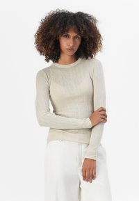 Langermet genser i lys beige ribbet stoff med rund hals og tettsittende silhuett, komplementert av subtile teksturdetailler.
