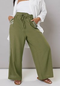 Olivgröna vida byxor med elastisk midja och dragsko. Har broderade blommönster på fickorna. Lättviktig tyg.