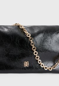 Zwarte leren clutch met een gekreukte textuur, voorzien van een gouden kettingband en een gouden logo-detail aan de voorkant.