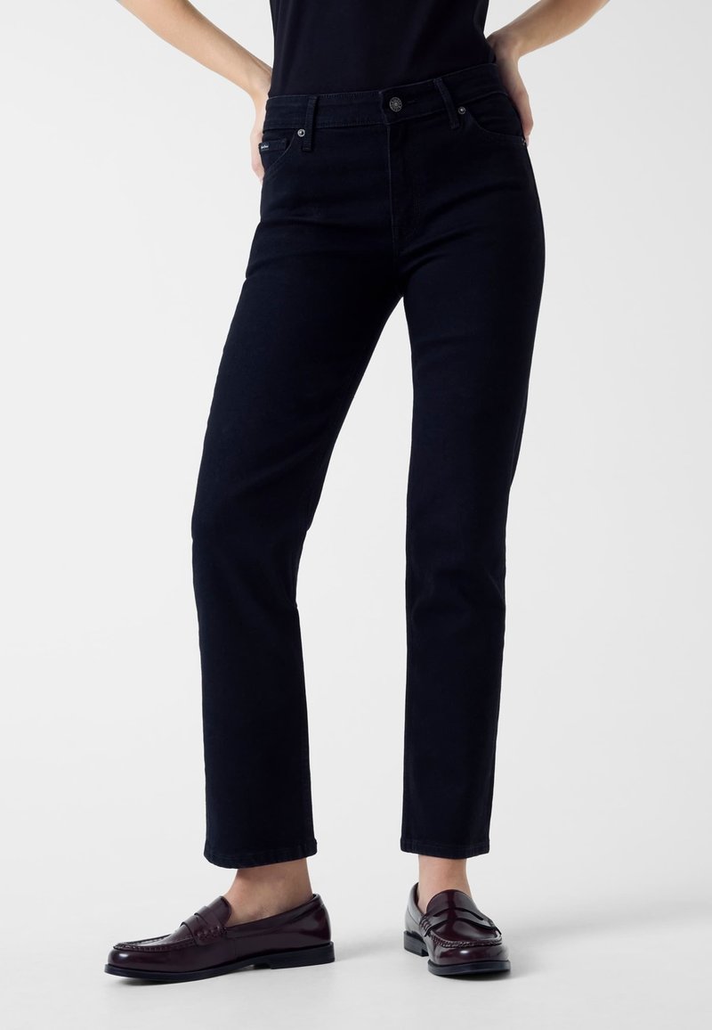 Jeans blu scuro a vestibilità slim, con tasche anteriori, chiusura con cerniera e bottone. Indossati con mocassini scuri.