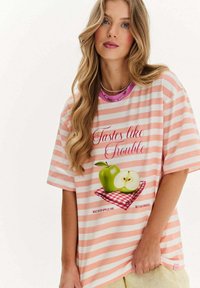 Mladá žena s dlhými blond vlasmi má na sebe ružovo-biele pruhované tričko s zelenými jablkami a textom "Chutí ako problémy".