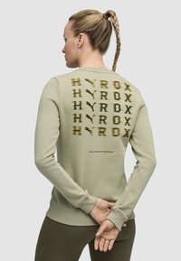 Felpa verde chiaro con un audace logo "HYROX" ripetuto in verde scuro sulla schiena, con polsini e orlo a coste.