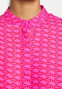 Fuksjowa koszula z kołnierzykiem, listwą guzikową i powtarzającym się wzorem ciemniejszych różowych ogniw na całej tkaninie.