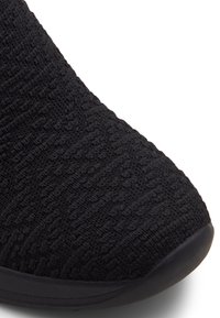 Chaussure de sport noire avec une tige en maille texturée, un bout arrondi et une semelle flexible. La surface présente un motif en maille.