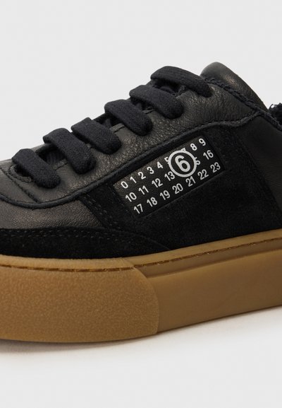 Svarta sneakers med läder- och mockamaterial, runda snörning, gummisula och en sidodekal med siffror i ett rutmönster.