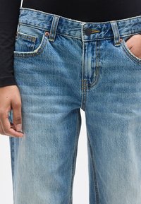 Ανοιχτό μπλε τζιν παντελόνι με ίσια γραμμή, που διαθέτει μπροστινές τσέπες, εμφανή ραφές και ελαφρώς ξεθωριασμένο φινίρισμα.