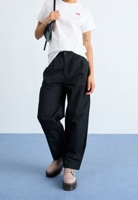Zwarte oversized broeken met een knoopsluiting, gecombineerd met een witte t-shirt met een klein roze logo, en lichtroze veterschoenen.
