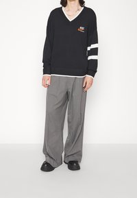 Person wearing black Nike sweater with white stripes on sleeve, gray wide-leg trousers, black shoes, and a silver chain necklace.