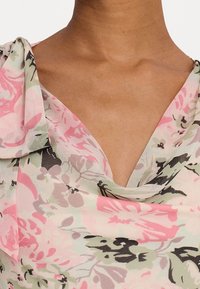 Floral sleeveless dress in lightweight fabric features soft, draped neckline. Colors include pink, green, and black patterns on a light background.