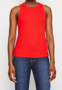 Rode geribbelde tanktop met een ronde halslijn en mouwloos ontwerp. Bevat een subtiele logo-accent nabij de zoom. Gemaakt met blauwe jeans.