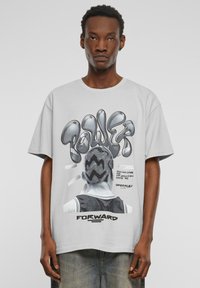 Gray oversized t-shirt featuring a graphic of a person with a unique hairstyle, bold "POWER" text, and text elements. Soft fabric texture.