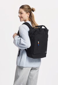 Zaino nero realizzato in tessuto resistente, dotato di manico superiore, spallacci regolabili e una tasca frontale con zip e dettagli colorati.