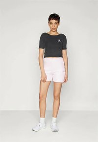 Μαύρο κοντό μπλουζάκι με λογότυπο, ροζ σορτς, λευκά αθλητικά παπούτσια και λευκές κάλτσες. Απλός σχεδιασμός με χαλαρή εφαρμογή, κατάλληλο για καθημερινή χρήση.