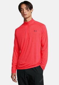 Rood langwerpig sweatshirt met een halve ritssluiting bij de kraag, voorzien van een textuurstof en een zwart logo op de linkerborst.