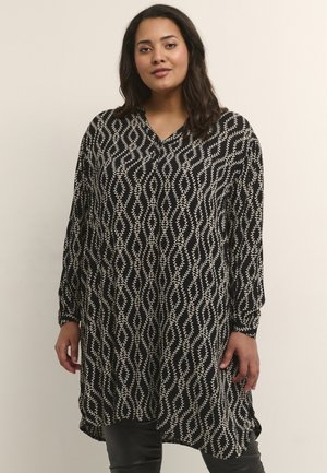 Tunique noir et blanc présentant un motif ondulé, des manches longues, un col en V et une coupe décontractée avec une légère fente sur le côté au niveau de l'ourlet.