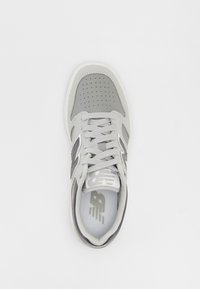 Šedá a bílá teniska New Balance s tkaničkami, perforovanou špičkou a logem na boku a stélce, pohled zhora na bílém pozadí.