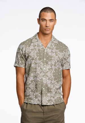 Chemise à manches courtes en tissu olive, présentant des motifs de paisley blancs et des points, avec une coupe décontractée et un col classique.
