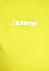 Ljust gul passformad skjorta i ribbad väv, med en vit "hummel"-logotyp som är tydligt synlig.