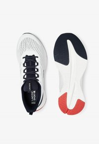 Vita idrottsskor i vitt med överdel i mesh, svarta detaljer och röda inslag på yttersulan. Utrustad med snörning och strukturerad sula för grepp.