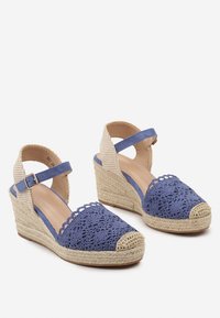 Sandales compensées en crochet bleu avec une semelle en jute tressé, une bride adjustable à la cheville et un bout rond, présentant un dessus texturé et des accents beiges.