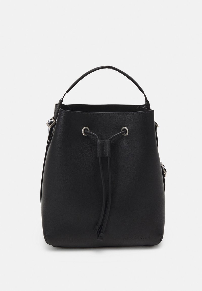 Sac seau en cuir noir avec une seule poignée supérieure et une fermeture par cordon à l'avant, œillets argentés et design minimaliste.