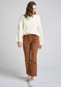 Pull blanc texturé avec des manches ballon, associé à un pantalon en velours côtelé marron à pattes d'éléphant et des baskets blanches. Taille ajustée avec un détail de bouton.