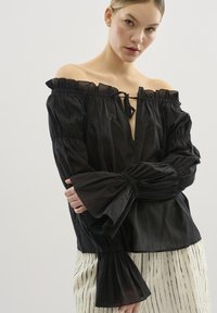 Schwarze schulterfreie Bluse mit gefältelten langen Ärmeln, V-Ausschnitt und Kordelzug für eine verstellbare Passform. Glatte Textur.