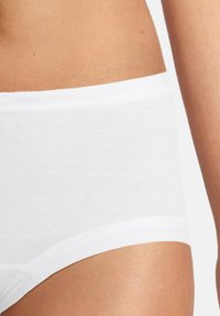 Slip di cotone bianco con una texture liscia, dotato di una fascia medio-alta e un taglio classico, che lascia intravedere parte dell'anca e della pelle.